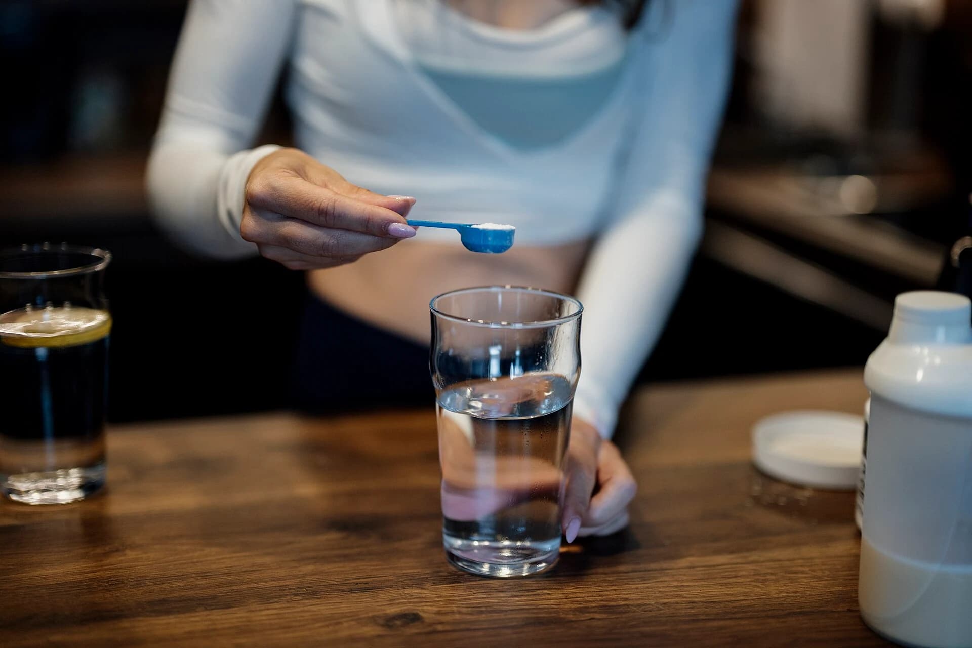A scoop of white supplement powder held over a clear glass of water